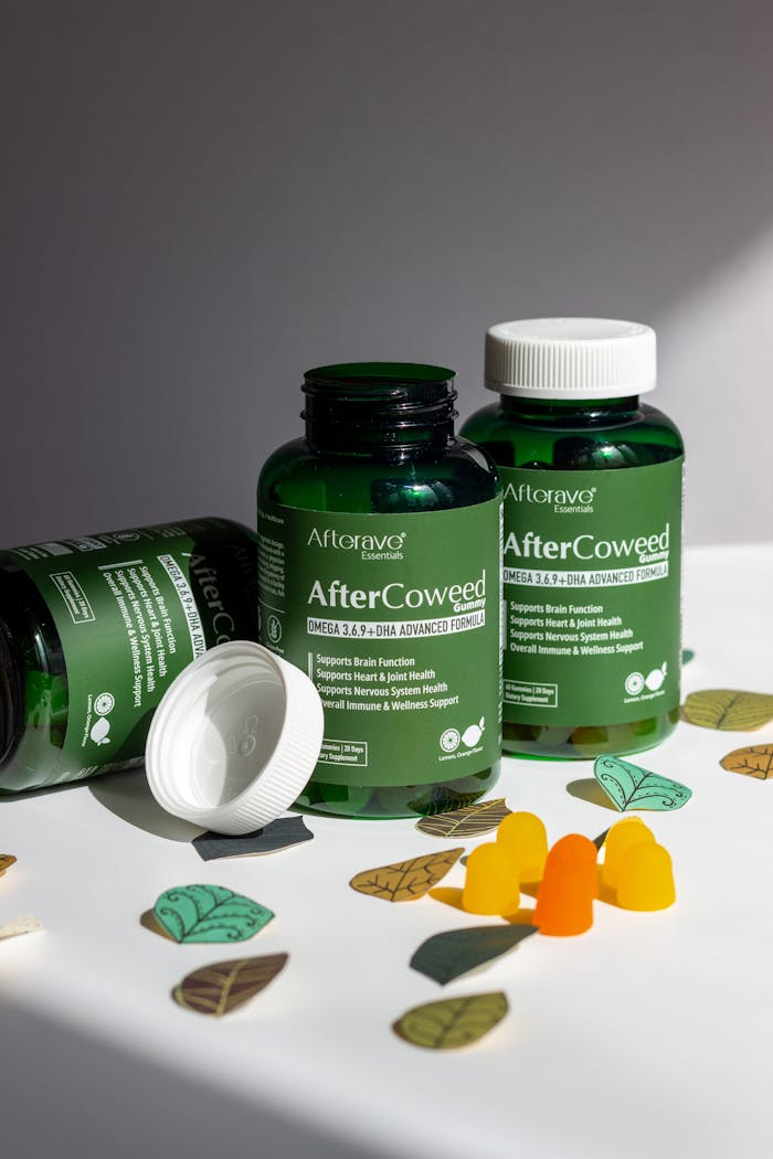 Green supplement bottles labeled 'AfterCoweed' with gummies and leaves on a white surface